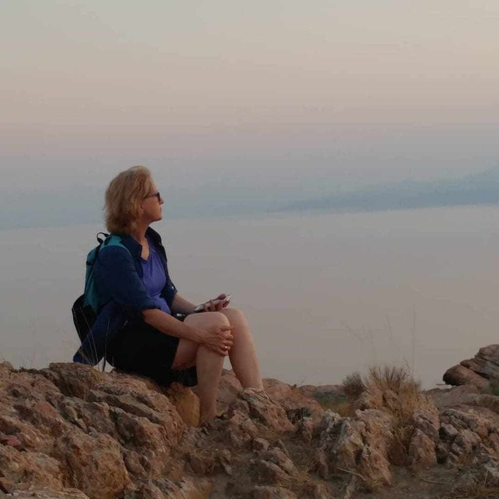 Kim Allchrch Flick sits on a rock during a hike. She's looking over a body of water.